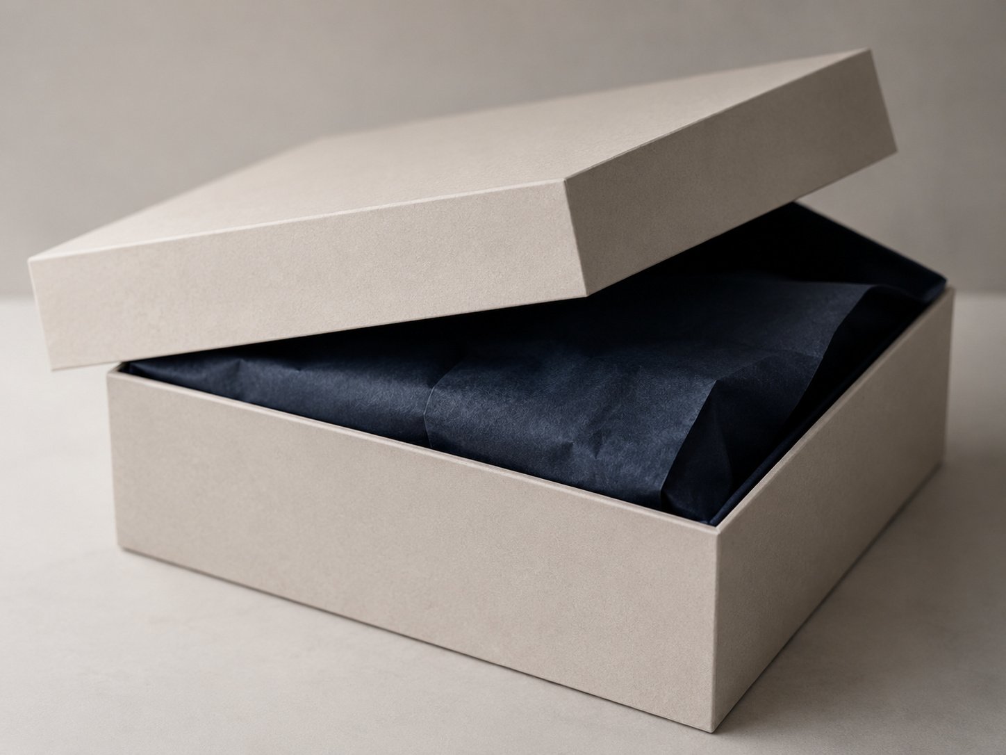 Rigid box lid lifted to reveal a dark colored interior lining and tissue paper